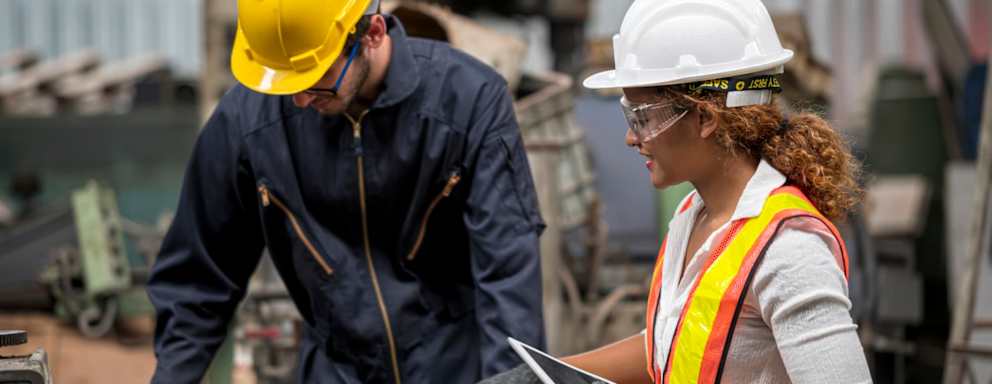 Female Machinery Engineer and male technical in safety protective wear while discuss with using tablet computer. They standing near CNC milling machine.