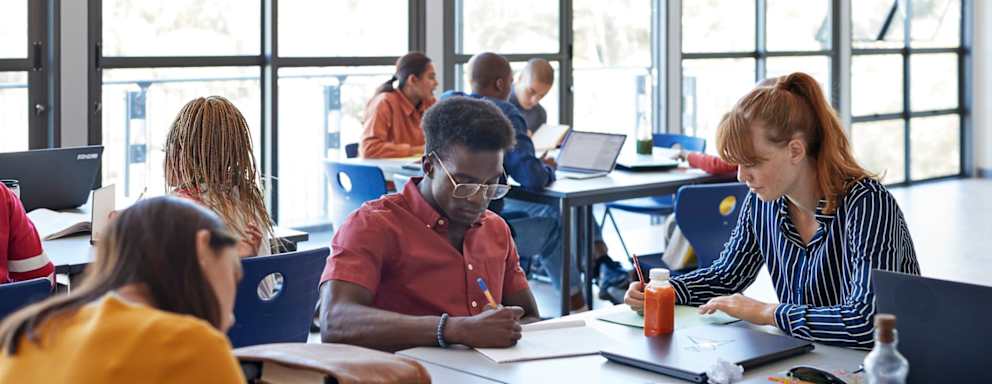 Young female and male university students studying while sitting on desk in classroom