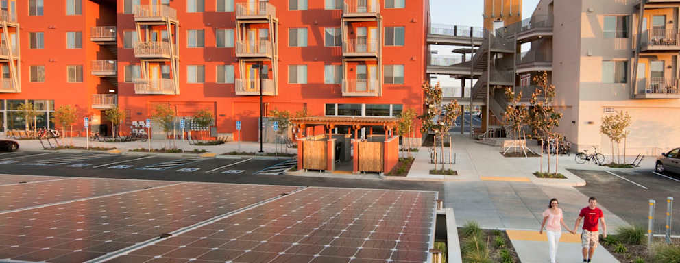 Two persons walking near green buildings on UC Davis campus.