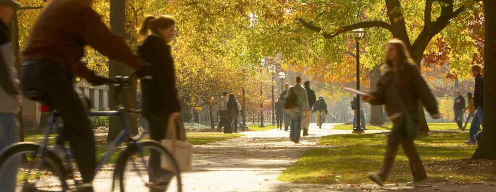 Students walking and biking on the campus footpaths at the University of Michigan Ann Arbor on a sunny autumn day.