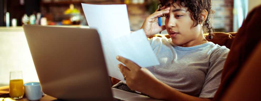 Woman sitting on her living room couch at home. She is using her laptop while paying off student loan bills.