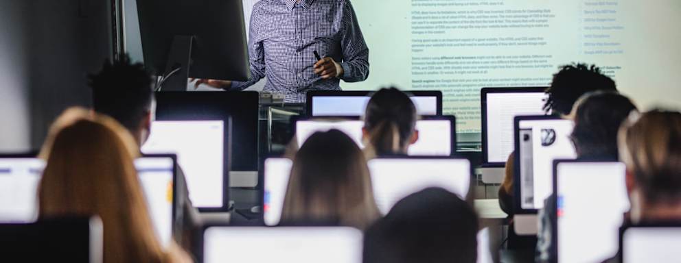 Male teacher giving a lecture from desktop PC during a class at computer lab.