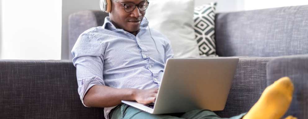 Young man sitting on the floor in the living room using laptop and headphones