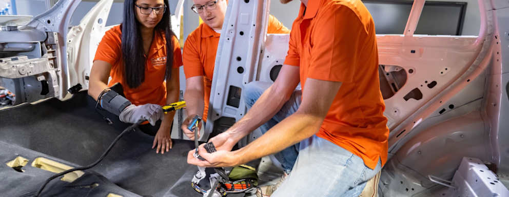 Clemson Launches Nations First Bachelor of Science in Automotive Engineering. Students wearing orange polo shirts working on the interior of a car.