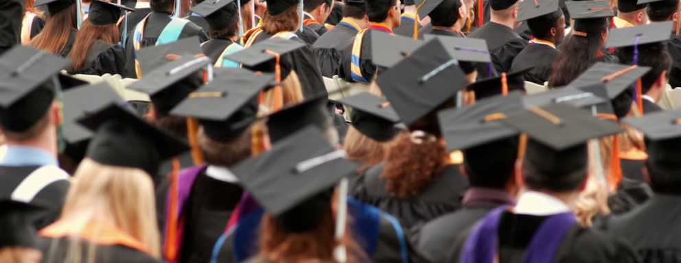 A group of graduates at their graduation ceremony. they are all wearing a cap and gown and are all standing.
