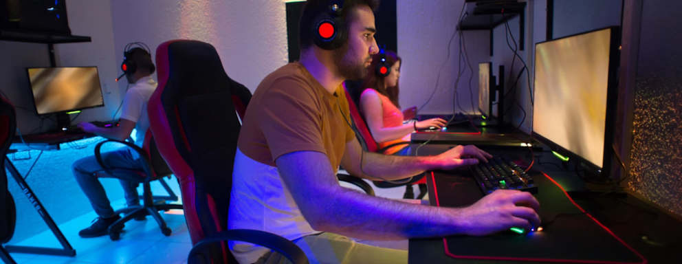 Young gamers wearing gaming headphones with backlight and playing computer video games in dark gamers club.