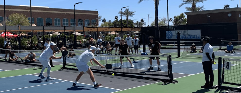 A group of people wearing white clothing playing pickleball on a bright sunny day.