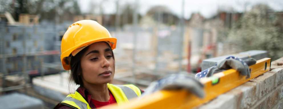 Female construction worker using level tool on brick wall