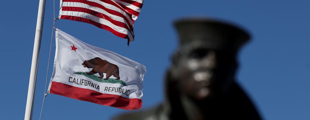 An American flag and the California State flag flying next to the Lone Sailor statue in Sausalito, California.