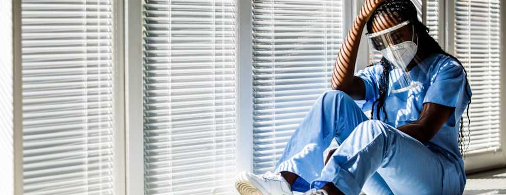 Overwhelmed nurse wearing PPE sitting down in a hospital hallway