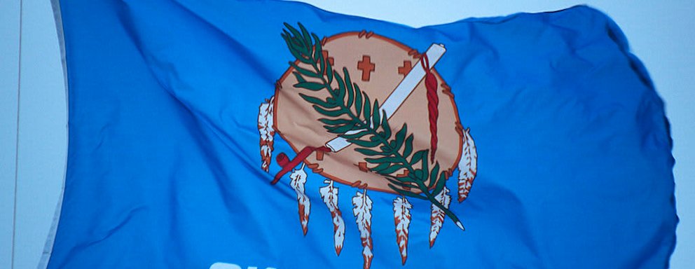 The state flag of Oklahoma flying in the wind on a sunny day.