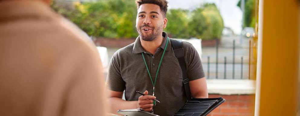 Black male social worker holding a clipboard and pen makes a house call to a client.