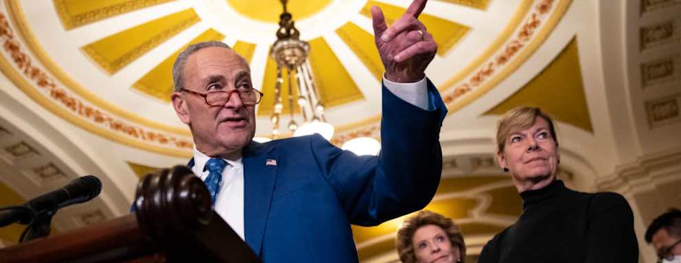 Senate Majority Leader Chuck Schumer speaking to reporters after a policy meeting with Senate Democrats at the U.S. Capitol in Washington, DC. Also pictured in the background are Senators Debbie Stabenow and Tammy Baldwin.