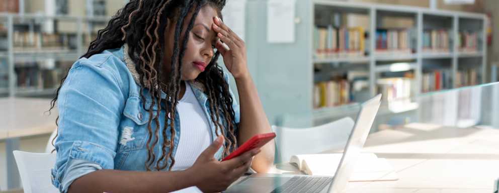 Black female student applying to college on her laptop. She is resting her head on her left hand, with a frustrated look on her face.