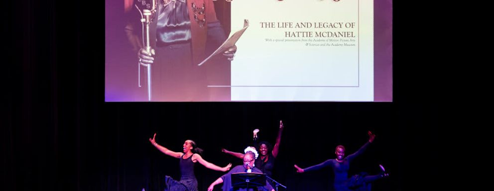 Stage performance with "Hattie Comes Home" on screen