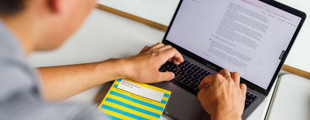 A college student sits in front of a laptop and uses an AI chatbot to help him complete a German language assignment.