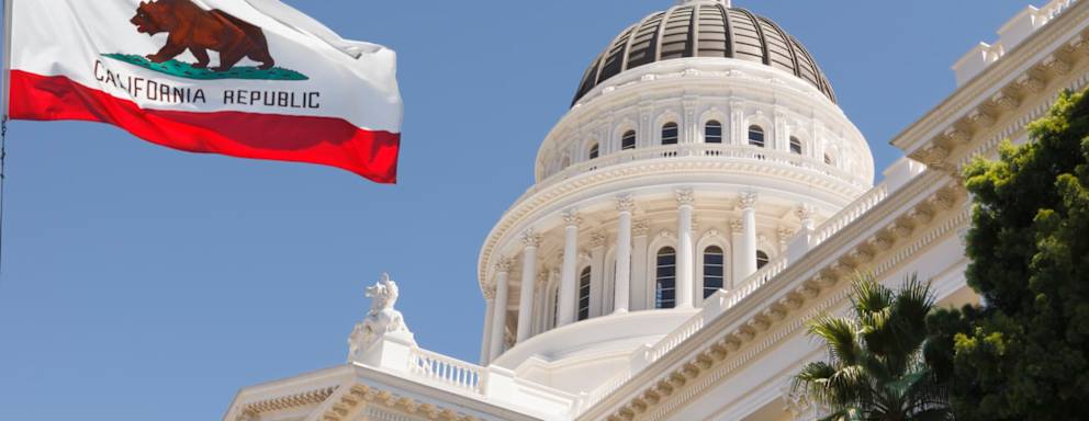 California State Capitol building with state flag in Sacramento on a windy summer day with clear sky.