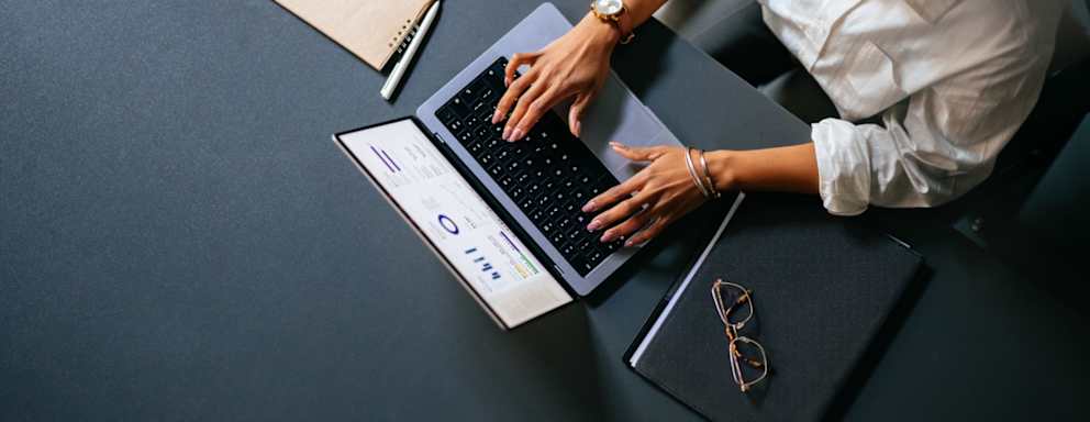 High Angle View Of Unrecognizable Woman Typing Business Report On A Laptop Keyboard In The Cafe