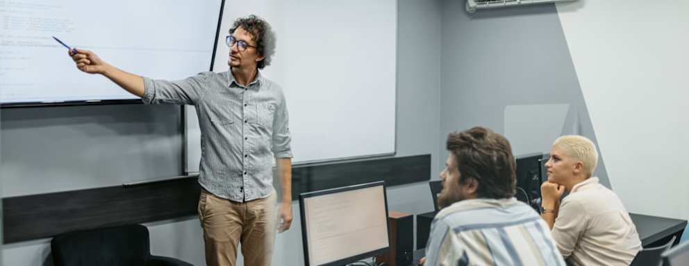 Young male teacher teaching young students a programming class in the classroom.