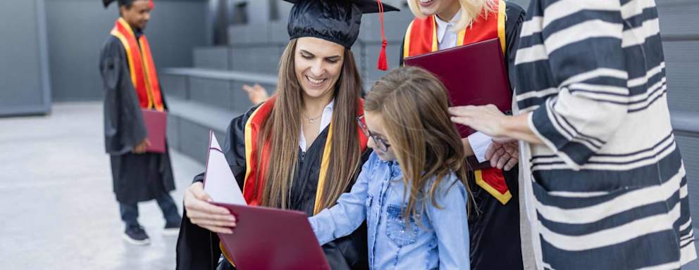 Female master's degree student in a wheelchair celebrating after her graduation ceremony with her daughter, family, and fellow graduates.