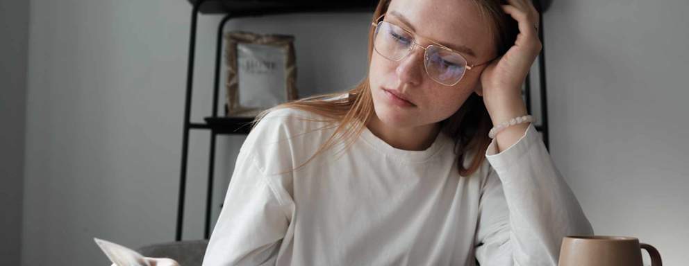 Stressed female college student sitting at her kitchen table at home. She is looking through receipts while trying to budget her monthly bills.