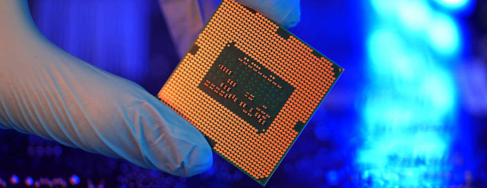 Close-up of a gloved hand holding a semiconductor microchip in a tech lab.