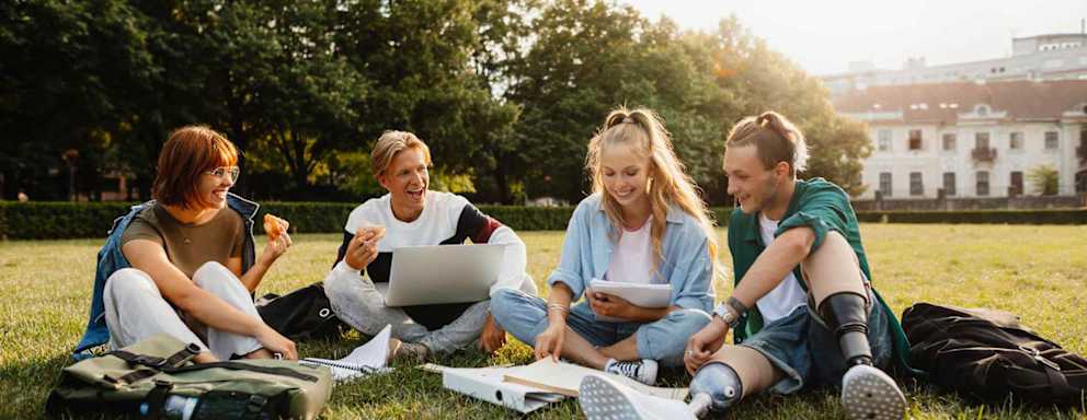 Friends sitting on grass outdoors in campus area.