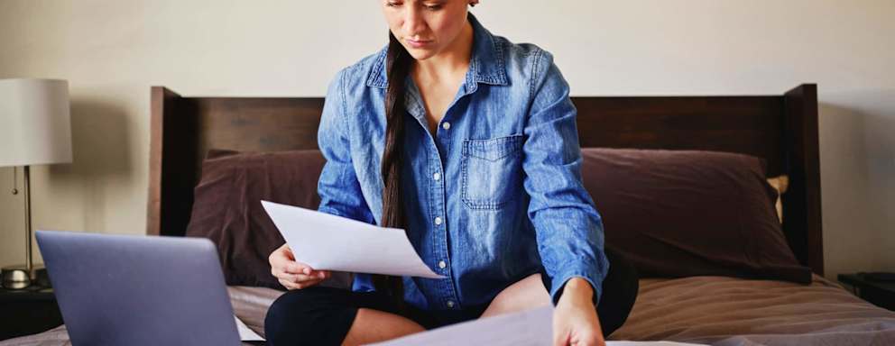 A woman sitting on her bed in a home looking through finances.