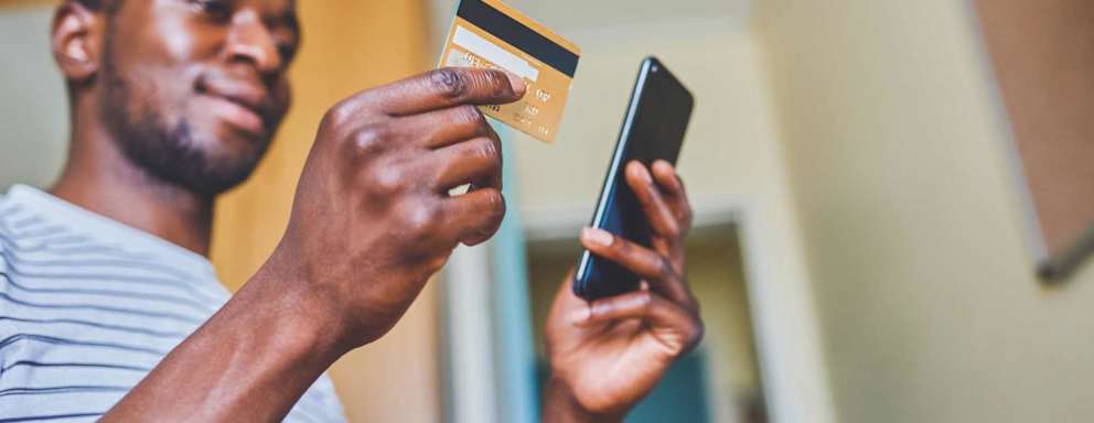 Cropped shot of a cheerful young man doing online shopping while using his cellphone and credit card inside of an apartment during the day