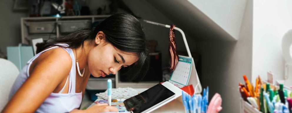 Teenage girl with headphones and laptop having online school class at home