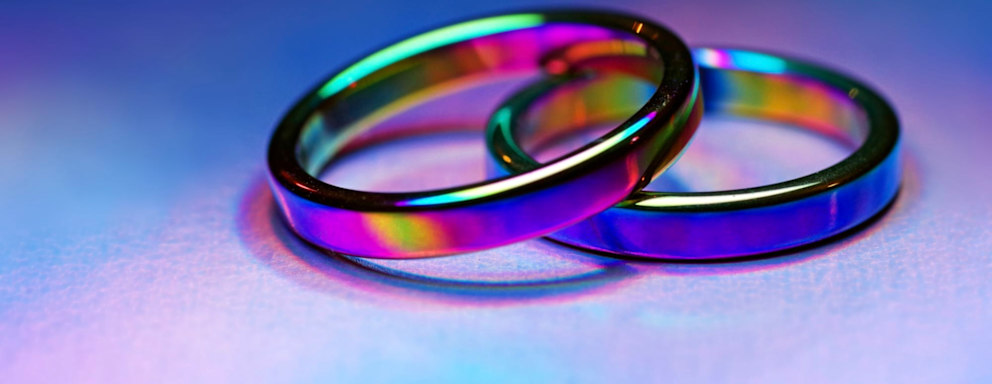 Two rainbow titanium-coated band rings on holographic foil paper with vibrant light effects