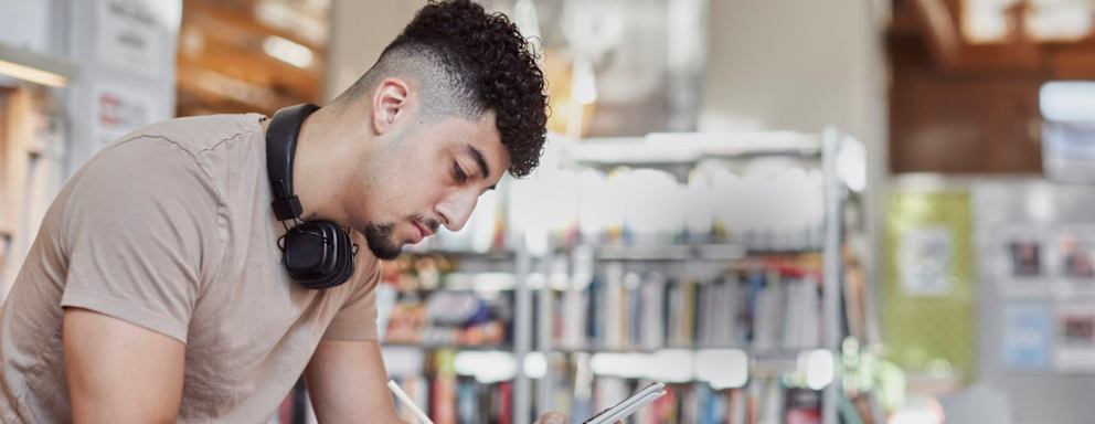 Male student taking notes in library.