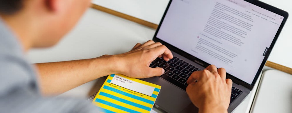 A college student sits in front of a laptop and uses an AI chatbot to help him complete a German language assignment.