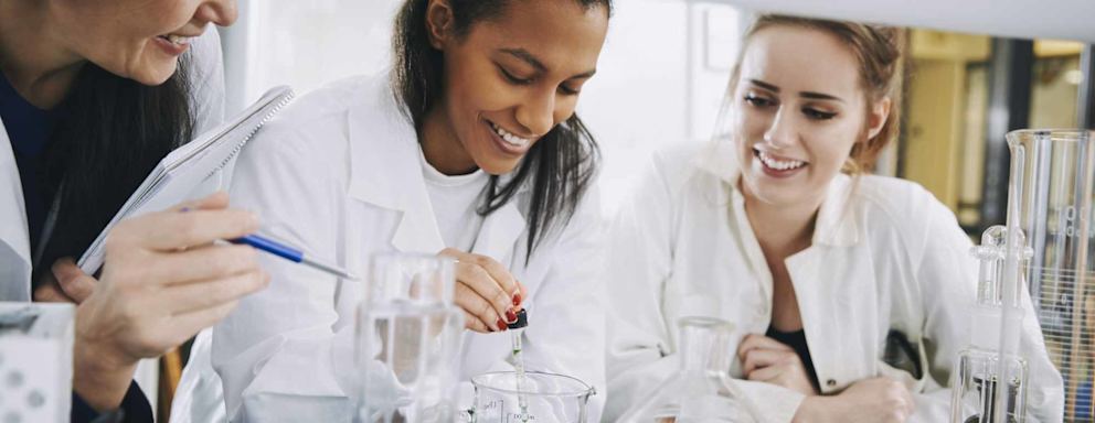 Smiling university students with mature teacher mixing solution in laboratory