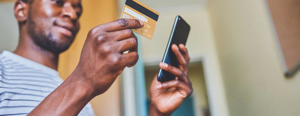 Cropped shot of a cheerful young man doing online shopping while using his cellphone and credit card inside of an apartment during the day