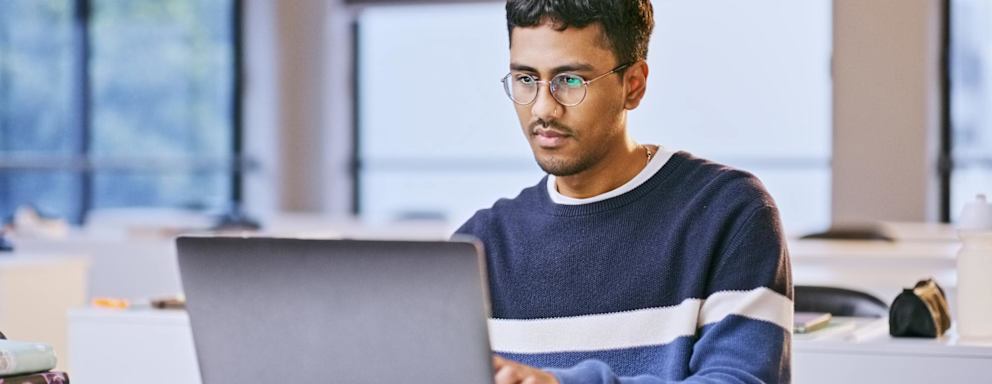 Laptop, university classroom and man reading online research study on history information, knowledge or education. School project, analysis and Indian student learning course for college development
