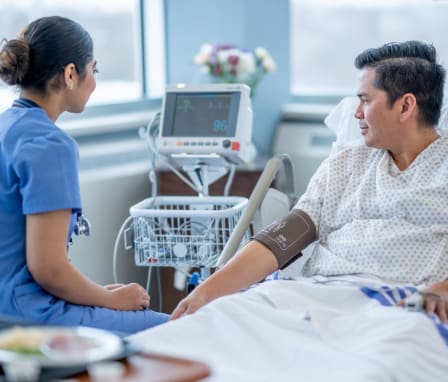 Nurse taking patient's blood pressure while in hospital bed