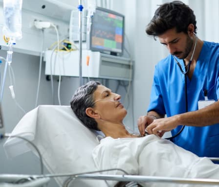 A male nurse is listening with a stethoscope the heart bit of a patient.