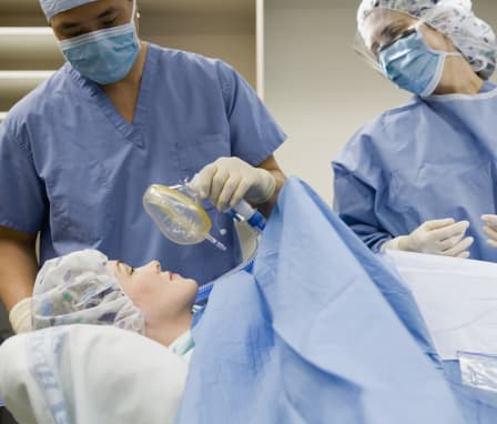 Nurse supplying patient with anesthesia beside surgeon