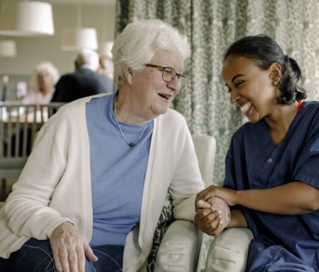 Cheerful female nurse holding hand of senior woman sitting at retirement home