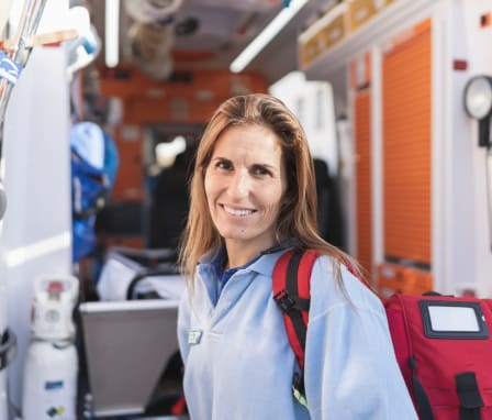 Woman paramedic smiling beside an ambulance with open doors