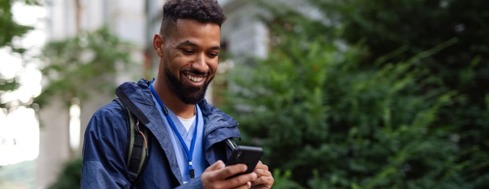 Male nurse outdoors in street on the way to work, using a phone, smiling