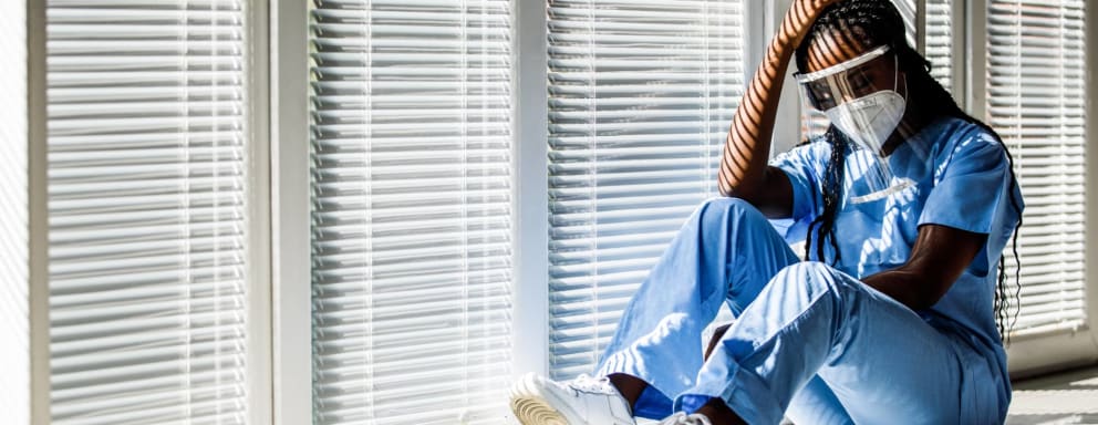 Overwhelmed nurse wearing PPE sitting down in a hospital hallway