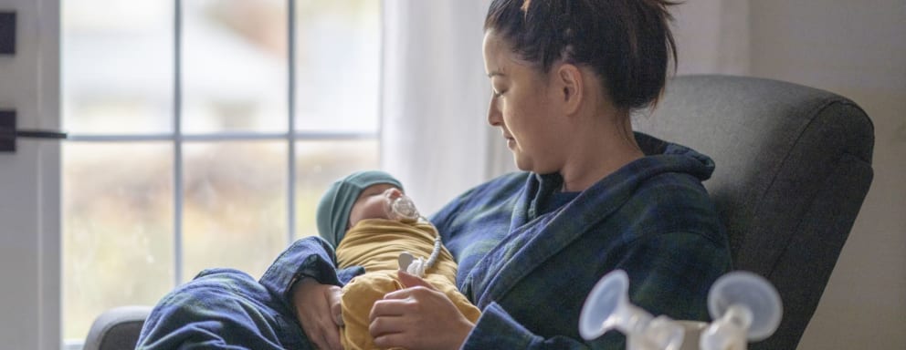 Mom holding newborn beside breast pump