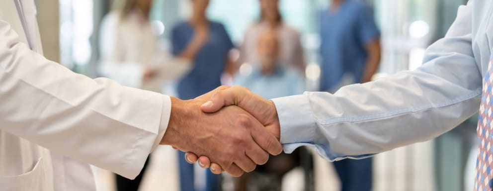 Medical professional shaking hands with business person, in front of medical team