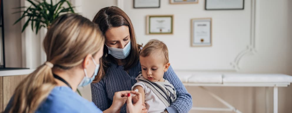 Nurse giving a vaccine to a baby in their mom's lap