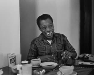 American novelist and activist James Baldwin sitting at a dining room table in his home.