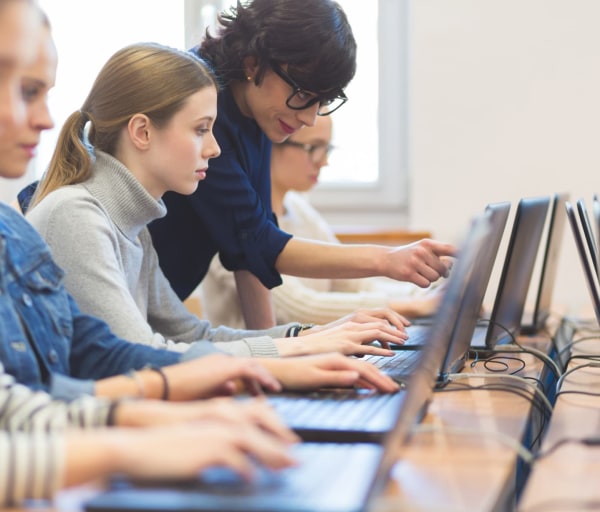 Students working on laptops with instructor helping