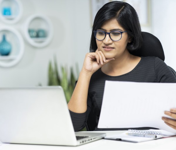 Woman working on laptop holding papers
