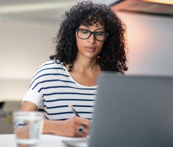 Woman taking notes while looking at laptop